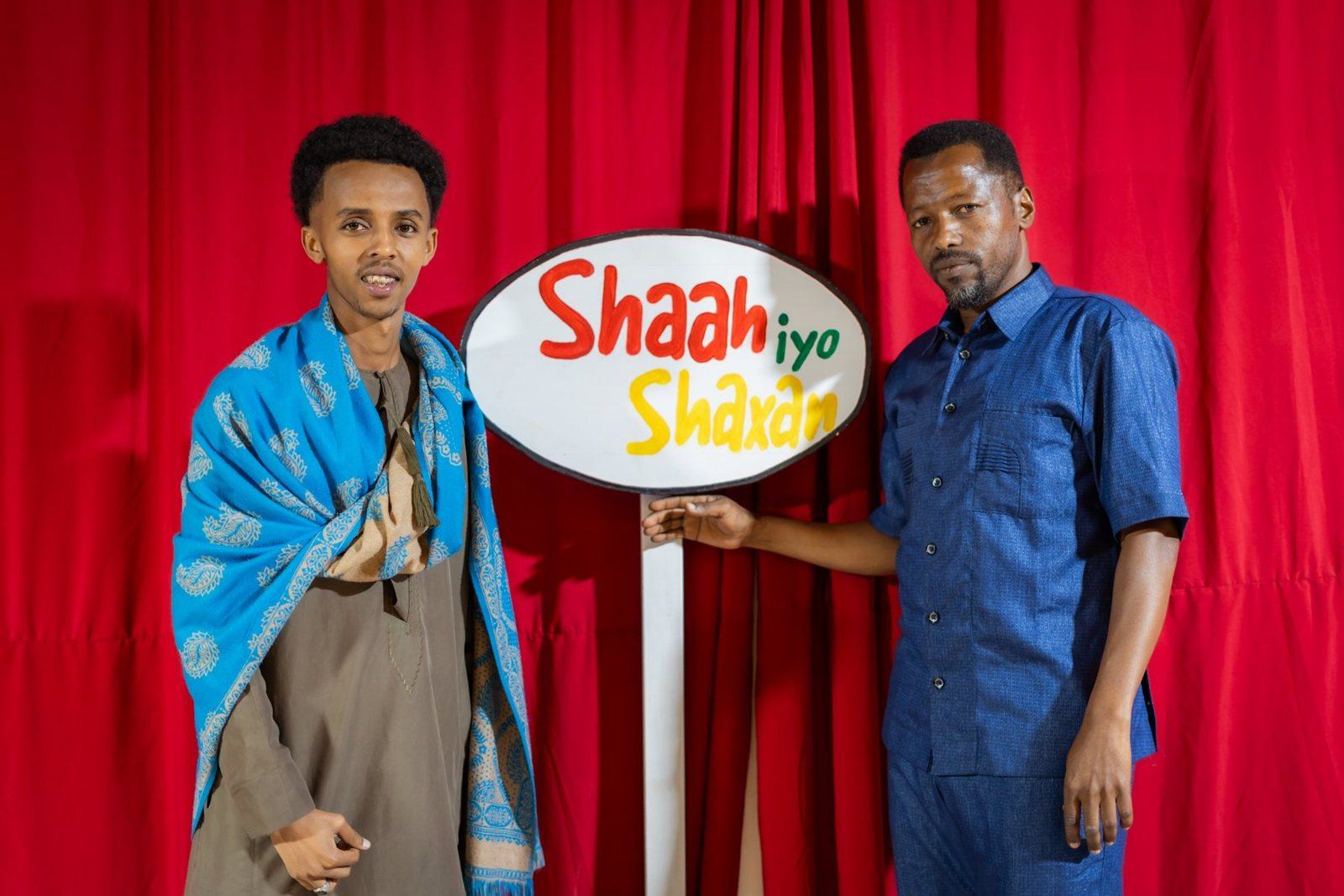 Host and guest in front of the Shaah iyo Shaxan sign