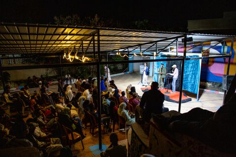 An evening talk on the stage in the creative courtyard, with a full audience under the string lights