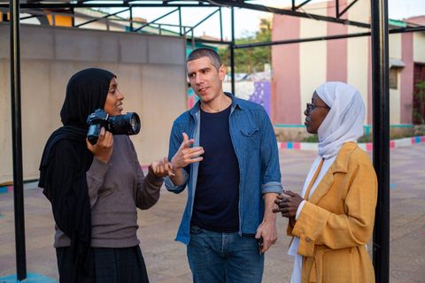 A visitor with a camera talks with two young women in the courtyard